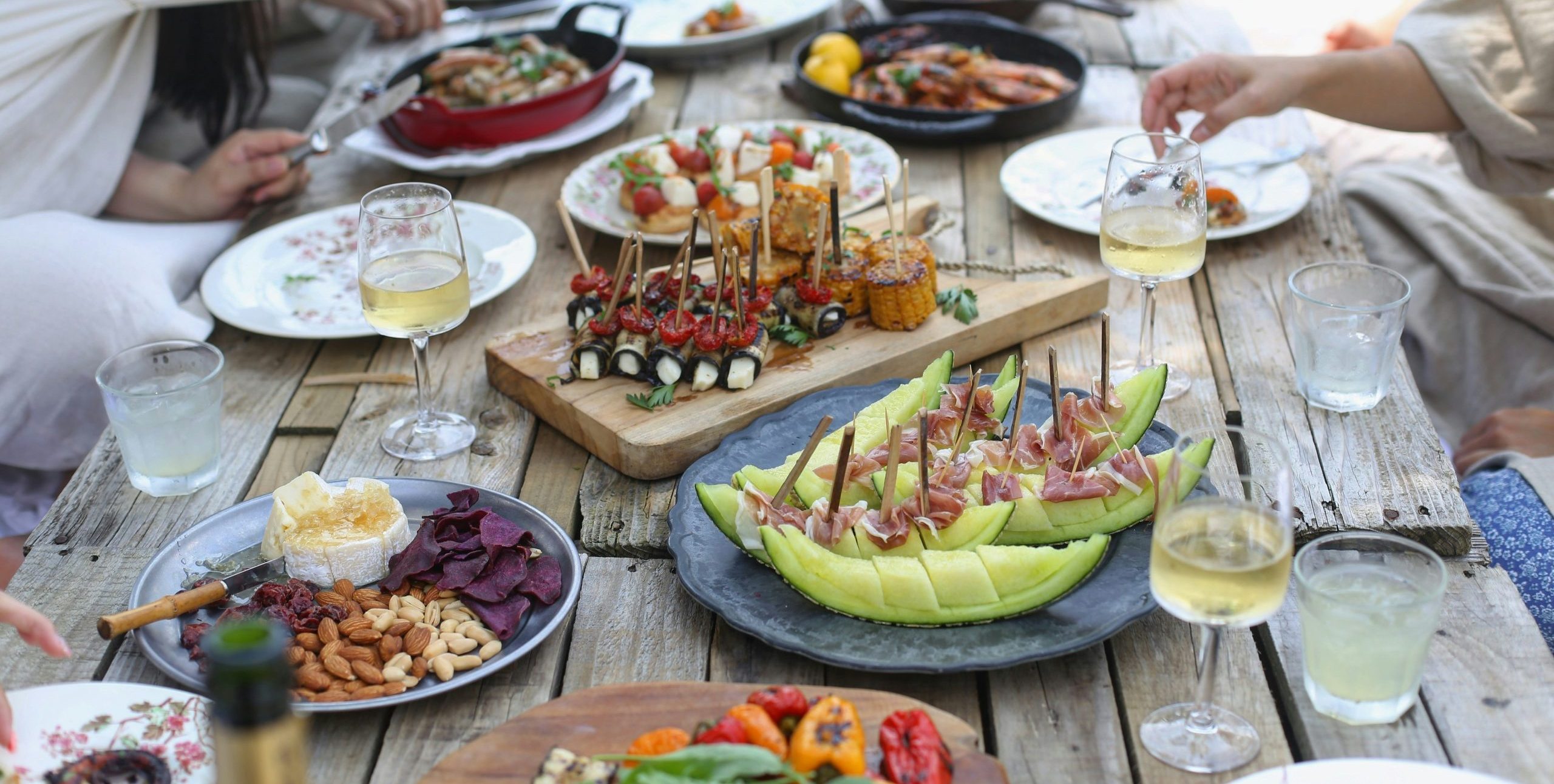 Image of people gathered around a picnic table filled with fresh tapas and crisp white wine